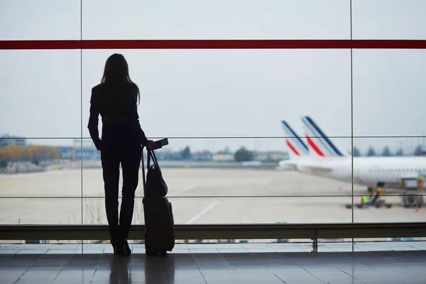 공항의 젊은 여자가 창문을 통해 비행기를 바라보고 있습니다 — 스톡 사진
