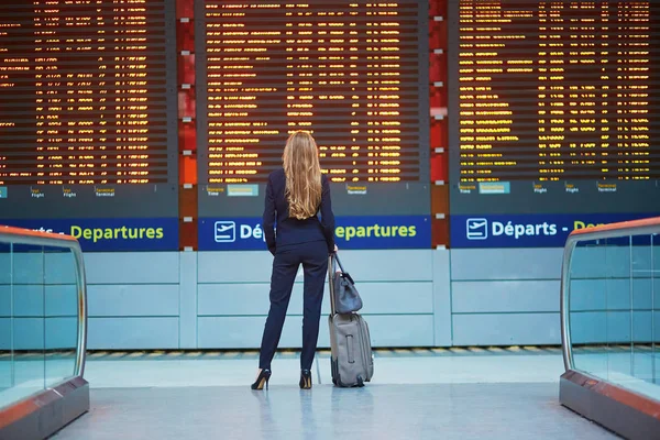 年轻女子在国际机场看飞行情报板上，检查她的航班 — 图库照片