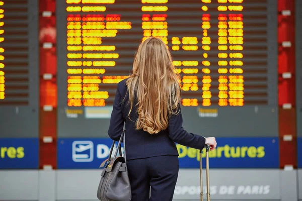 Junge Frau auf dem internationalen Flughafen schaut auf die Fluginformationstafel und überprüft ihren Flug — Stockfoto