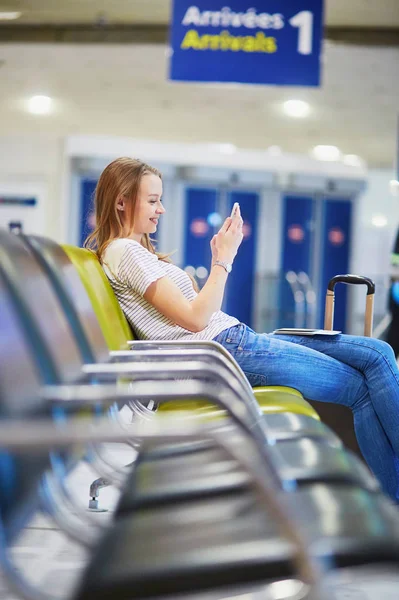 Mladí travelerin mezinárodní letiště kontrolu svého mobilního telefonu při čekání na její let — Stock fotografie