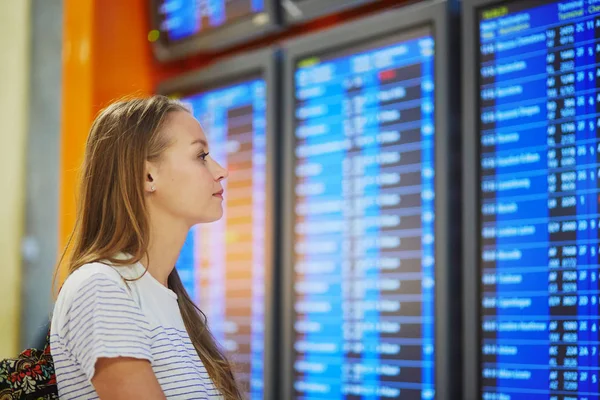 Jovem mulher no aeroporto internacional olhando para a placa de informações de voo — Fotografia de Stock