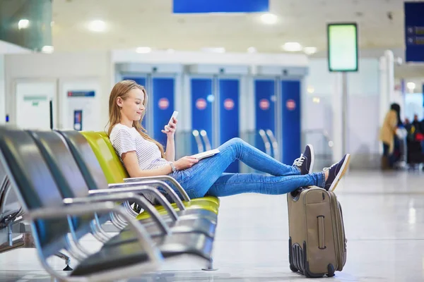 Young travelerin international airport checking her mobile phone while waiting for her flight — Stock Photo, Image