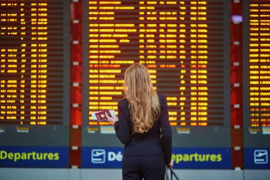 Woman with hand luggage in international airport terminal, looking at information board
