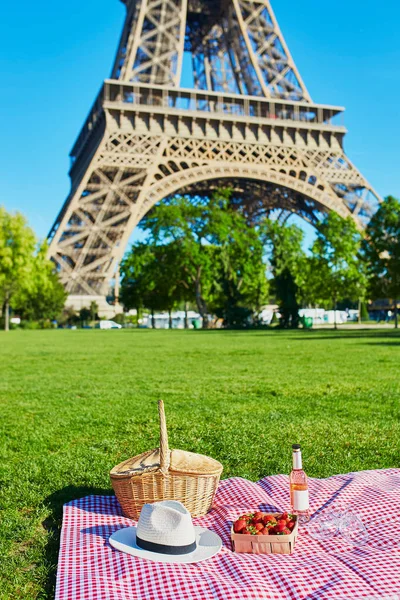 Conjunto de piquenique com cesta, vinho rosa, morangos e copos perto da torre Eiffel — Fotografia de Stock