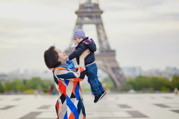 Madre lanzando a su pequeño hijo en el aire cerca de la torre Eiffel —  Fotos de Stock