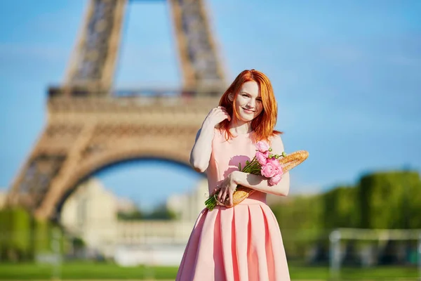 Meisje met traditioneel Frans brood (stokbrood) en bloemen voor de Eiffeltoren — Stockfoto