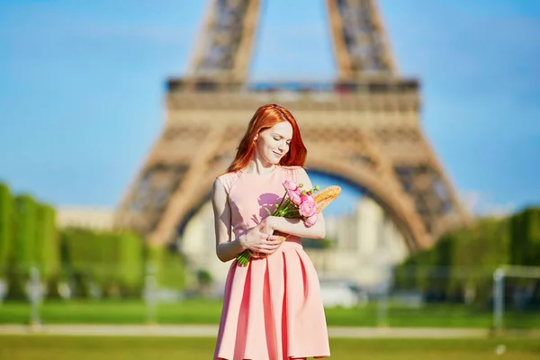 Meisje met traditioneel Frans brood (stokbrood) en bloemen voor de Eiffeltoren — Stockfoto