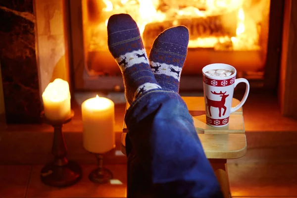 Piedi dell'uomo in calzini caldi con grande tazza di cioccolata calda e murshmallows vicino al camino — Foto Stock