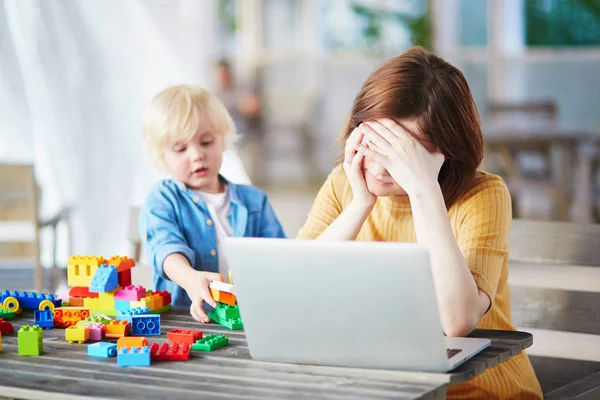 Mały chłopiec bawi budulec, podczas gdy jego matka pracuje na komputerze — Zdjęcie stockowe