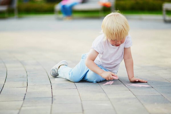 Little boy drawing with chalks on asphalt