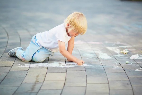 Kleiner Junge zeichnet mit Kreide auf Asphalt — Stockfoto