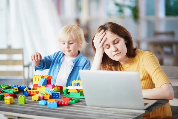 Мальчик играет со строительными блоками, пока его мать работает за компьютером — стоковое фото
