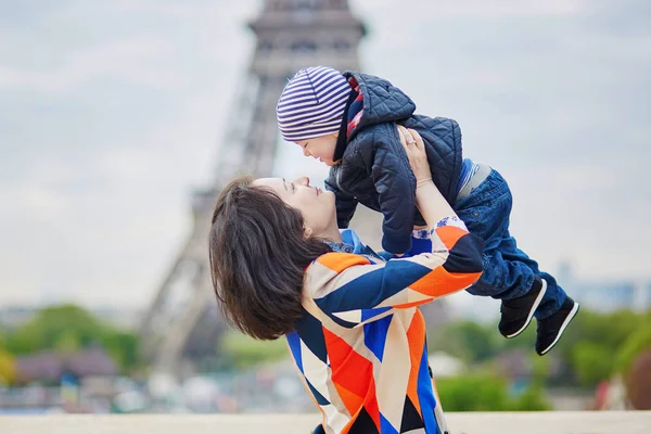 Madre lanzando a su pequeño hijo en el aire cerca de la torre Eiffel —  Fotos de Stock