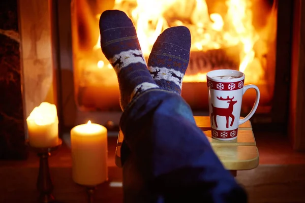 Pés de homem em meias quentes com grande caneca de chocolate quente e murshmallows perto da lareira — Fotografia de Stock