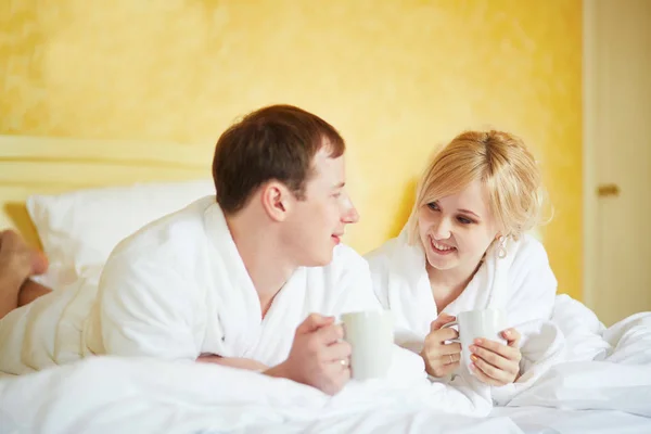 Echtpaar in witte badjassen drinken koffie samen in bed — Stockfoto