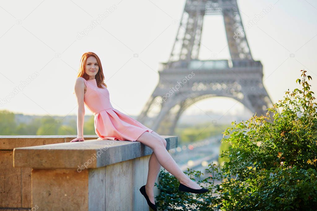 Beautiful young girl in pink dress near the Eiffel tower, enjoying her time in Paris, France