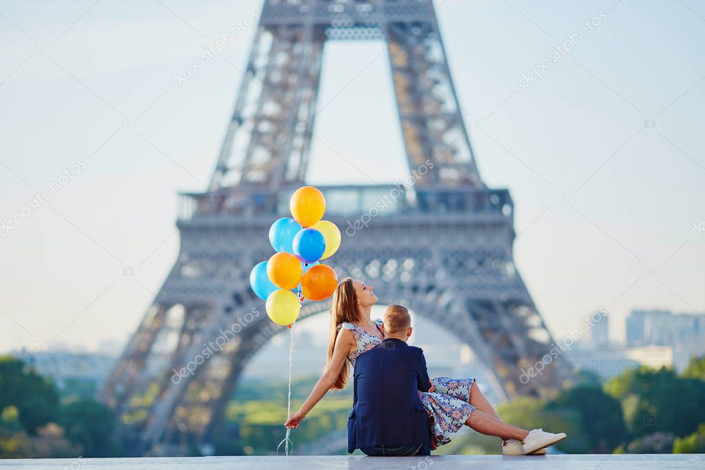 Loving couple with bunch of colorful balloons kissing near the Eiffel tower in Paris, France
