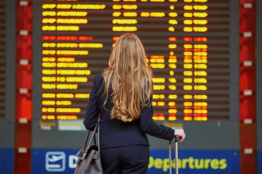 Onu uçuş kontrol bilgi tahtaya arıyorsunuz genç şık iş kadını Uluslararası Havaalanı terminal, el çantası ile. Kabin ekibi üyesi çanta.