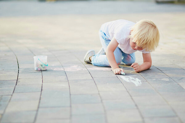 Adorable little boy drawing with colorful chalks on asphalt. Summer activity and creative games for small kids