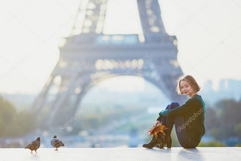 Beautiful young French woman with bunch of colorful autumn leaves near the Eiffel tower in Paris on a fall day