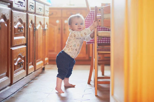 Baby Girl stående på golvet i köket och håller på att möbler — Stockfoto