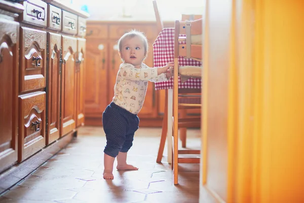Дитяча дівчинка стоїть на підлозі на кухні і тримається за меблі — стокове фото
