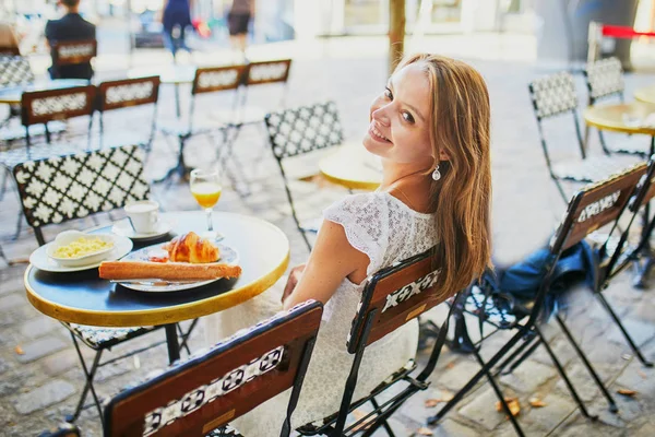 Vrolijke jonge vrouw ontbijten of brunchen in traditioneel Frans café — Stockfoto