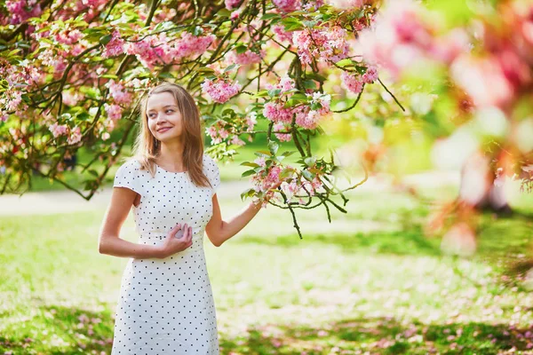 Jonge vrouw geniet van haar wandeling in het park tijdens kersenbloesem seizoen op een mooie lentedag — Stockfoto