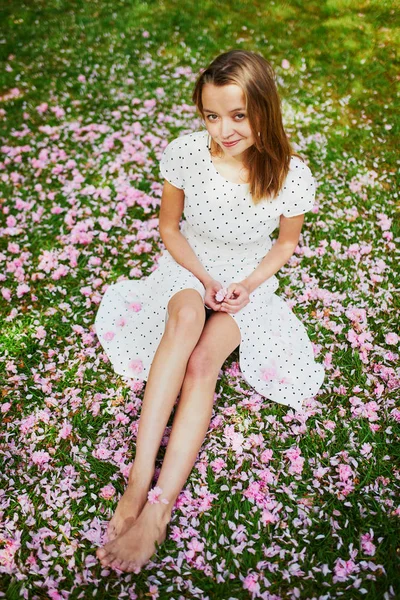 Mulher sentada na grama coberta com pétalas de cerejeira rosa e flores — Fotografia de Stock