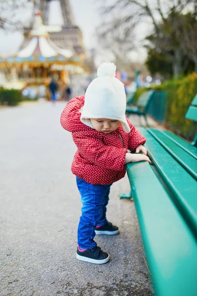 Baby girl standing on the street and holding on to bench — Stock Photo, Image