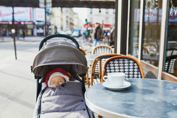 Mädchen schläft im Kinderwagen auf der Außenterrasse eines Pariser Straßencafés — Stockfoto