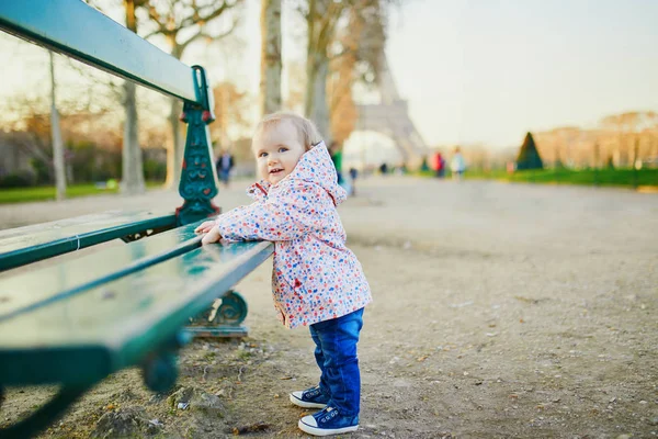 Niña de un año parada junto al banco cerca de la torre Eiffel — Foto de Stock