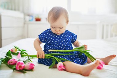 Mavi elbiseli kız pembe lalelerle oynuyor.