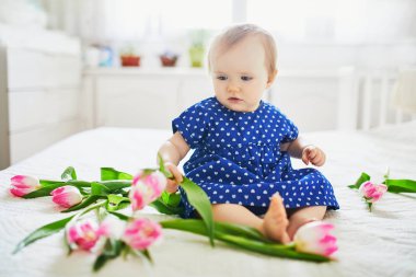 Mavi elbiseli kız pembe lalelerle oynuyor.