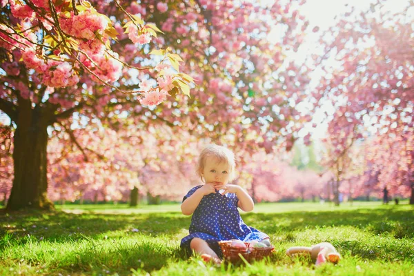 Süßes einjähriges Mädchen sitzt auf dem Gras und isst Erdbeeren — Stockfoto