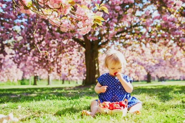 Roztomilé jeden rok stará dívka sedí na trávě a jíst jahody — Stock fotografie