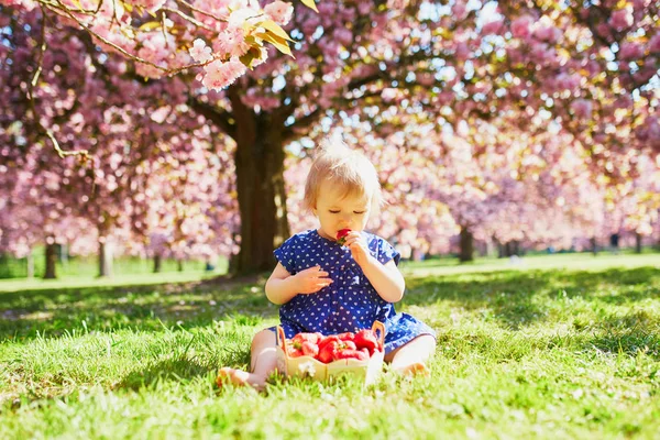 Roztomilé jeden rok stará dívka sedí na trávě a jíst jahody — Stock fotografie