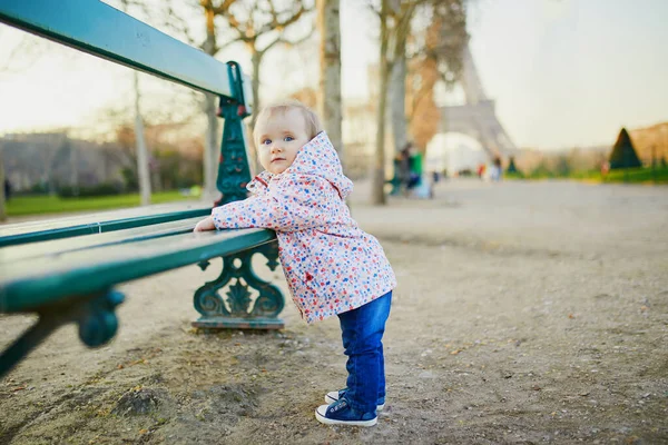 Niña de un año parada junto al banco cerca de la torre Eiffel — Foto de Stock