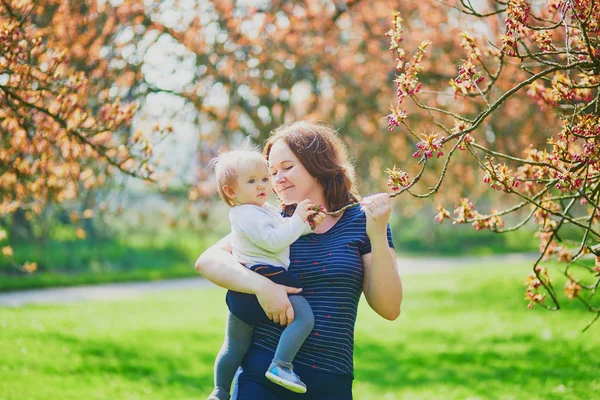 Mujer joven sosteniendo a su niña de 1 año en el parque en un día de primavera — Foto de Stock