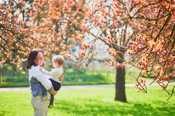 Middle aged woman holding 1 year old baby girl in park on a spring day — Stock Photo, Image