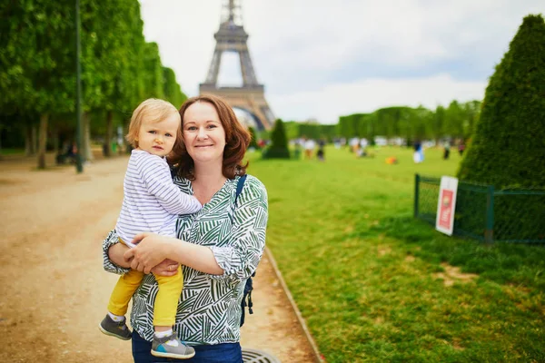 Счастливая молодая женщина держит своего годовалого ребенка возле Эйфелевой башни — стоковое фото