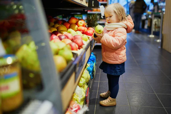 Очаровательная девочка в супермаркете выбирает яблоки — стоковое фото