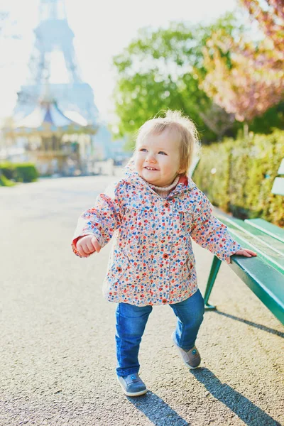 Niña de un año parada junto a un banco en París, con la torre Eiffel detrás de ella —  Fotos de Stock