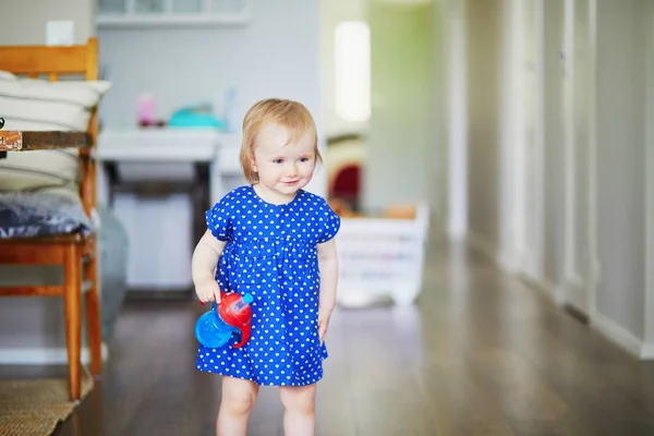 テーブルの上に彼女の水のボトルを置く青いドレスの女の赤ちゃん 家の小さな子供 — ストック写真