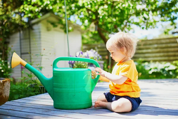 Sevimli bebek kız sıcak bir yaz günü sulama pot ile oynuyor. Küçük çocuk, ebeveynlere bahçeyle ilgilenmeleri için yardım ediyor. Serpme ile çocuk olabilir