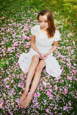 Çimenlerin üzerinde oturan bir kadın. Pembe kiraz ağacı yaprakları ve çiçeklerle kaplı. Bacakları yakın plan.