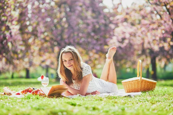 桜の季節に公園で晴れた春の日にピクニックをしている美しい若い女性 — ストック写真