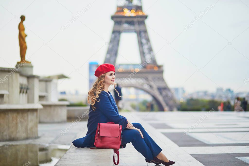 Young woman with long blond curly hair in Paris, France. Beautiful tourist in red beret near the Eiffel tower