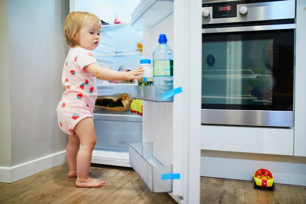 自宅で愛らしい幼児の女の子 冷蔵庫を開け 食べ物を選択 — ストック写真