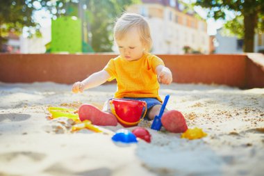 Sevimli küçük kız kum havuzunda oyun parkında eğleniyor. Bebek kum kalıplarıyla oynuyor ve çamur yapıyor. Çocuklar için açık hava yaratıcı aktiviteler